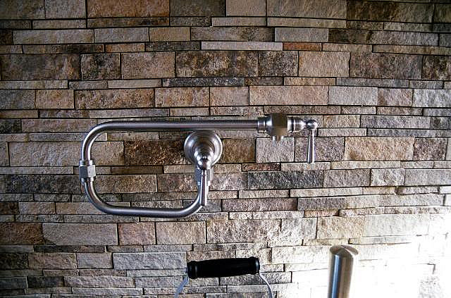 Stone backsplashes make an excellent backdrop to metal plumbing fixtures. (Image via Charlotte Granite Countertops on Flickr).